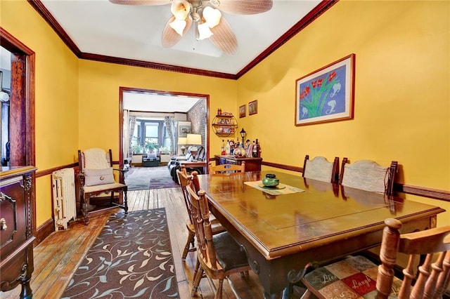 dining space with hardwood / wood-style floors, a ceiling fan, baseboards, radiator, and crown molding