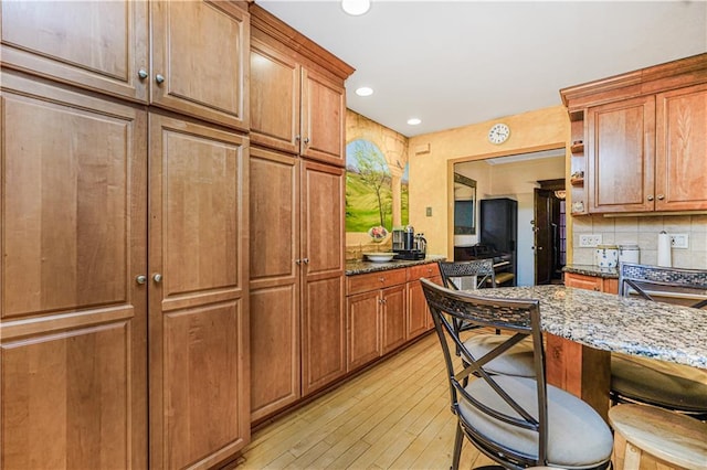 334 83rd St, Brooklyn, NY 11209 - kitchen with light wood-style flooring, dark stone countertops, backsplash, brown cabinetry, and recessed lighting