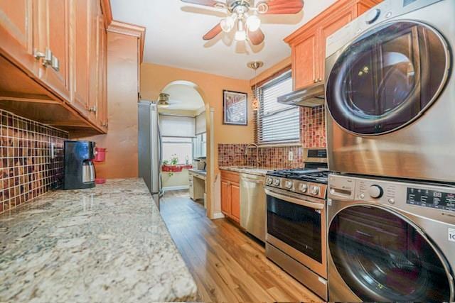 laundry area featuring stacked washer and clothes dryer, a ceiling fan, light wood-type flooring, arched walkways, and a sink