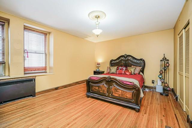 bedroom with radiator heating unit, wood finished floors, a closet, and baseboards