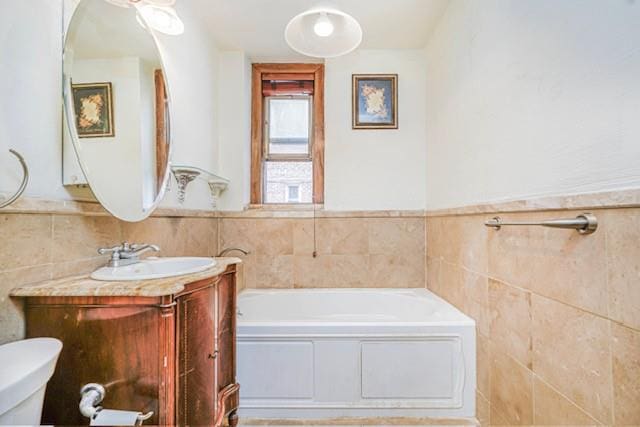 bathroom featuring tile walls, a bath, vanity, toilet, and wainscoting