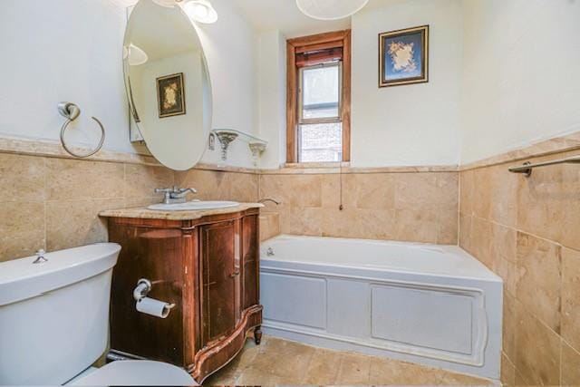 bathroom featuring tile walls, toilet, a bath, vanity, and wainscoting