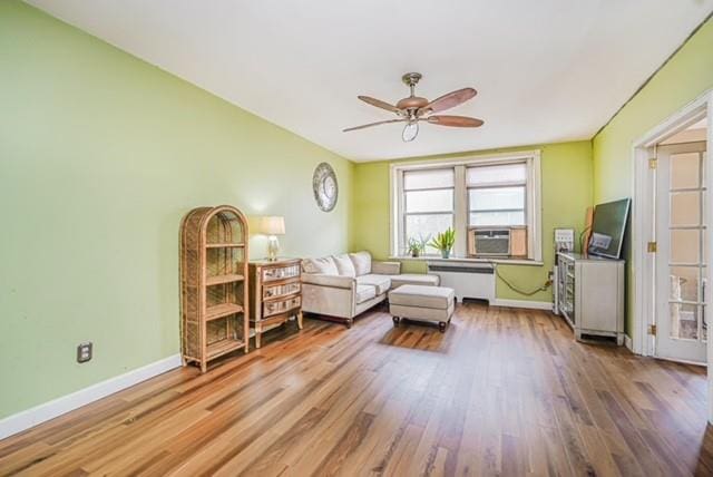 sitting room featuring a ceiling fan, wood finished floors, cooling unit, baseboards, and radiator