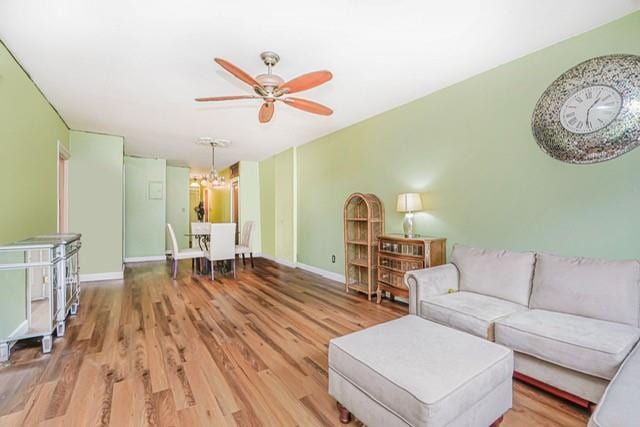 living room featuring a ceiling fan, a chandelier, wood finished floors, and baseboards