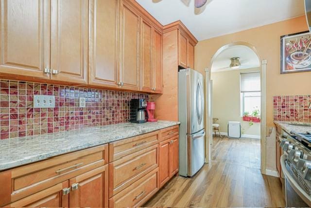 kitchen featuring appliances with stainless steel finishes, ceiling fan, light wood-style floors, and decorative backsplash