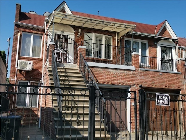 townhome / multi-family property featuring brick siding, a fenced front yard, a balcony, a gate, and ac unit