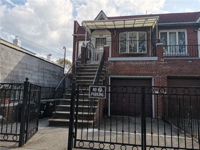multi unit property with brick siding, an attached garage, a fenced front yard, stairway, and a gate