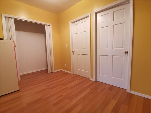 unfurnished bedroom with fridge, light wood-style flooring, and baseboards