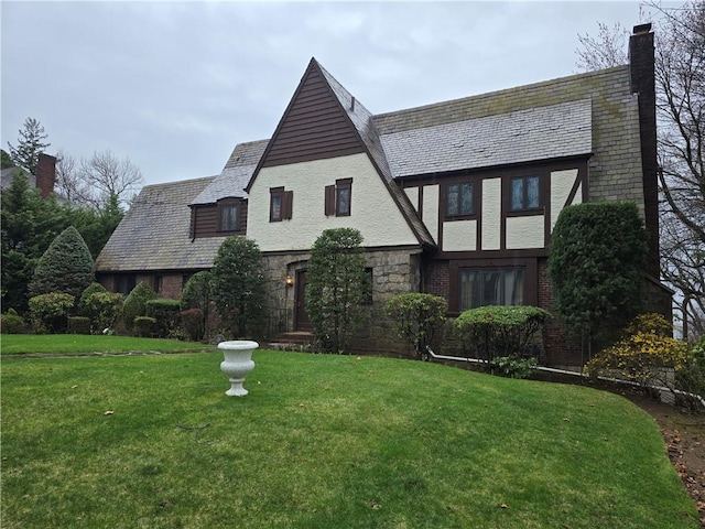 tudor house with a high end roof, a front lawn, stone siding, and a chimney