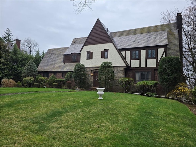 tudor home with a front lawn, a chimney, a high end roof, and stone siding