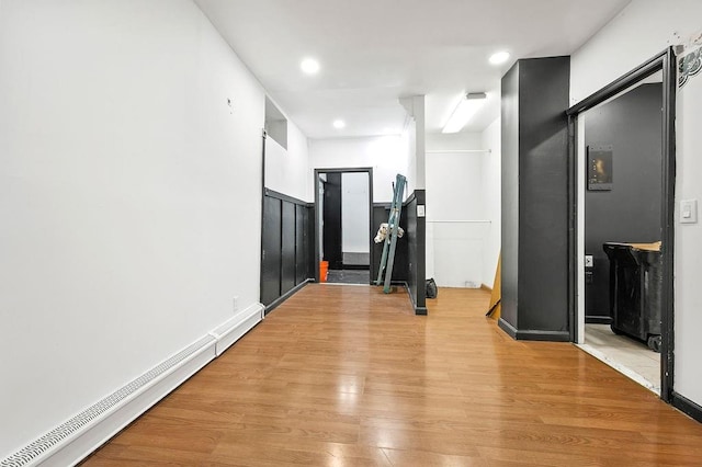 corridor with a baseboard heating unit, light wood finished floors, and recessed lighting
