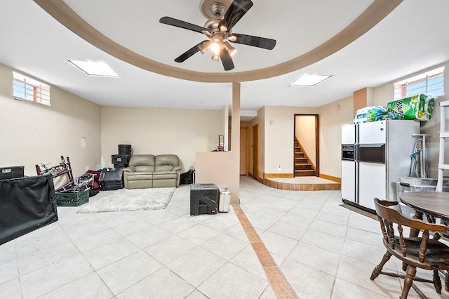 living room with light tile patterned flooring, a raised ceiling, stairway, and ceiling fan