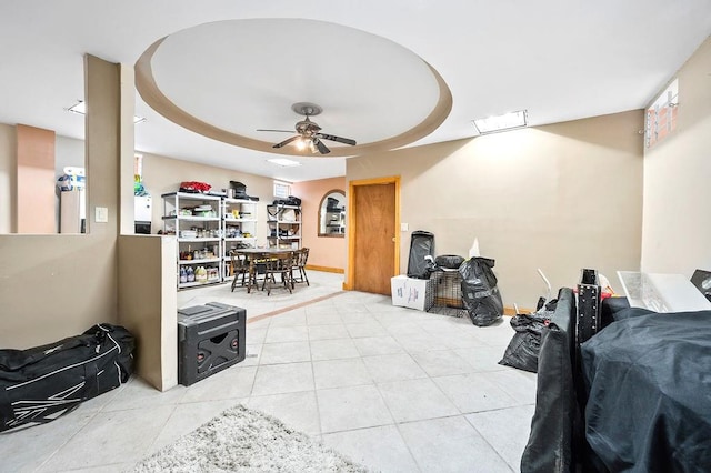 interior space featuring a raised ceiling, ceiling fan, baseboards, and light tile patterned floors
