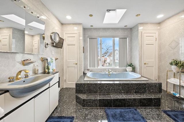 bathroom with a bath, tile walls, granite finish floor, a skylight, and vanity