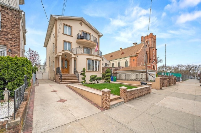 view of front of house with stucco siding, a balcony, and fence