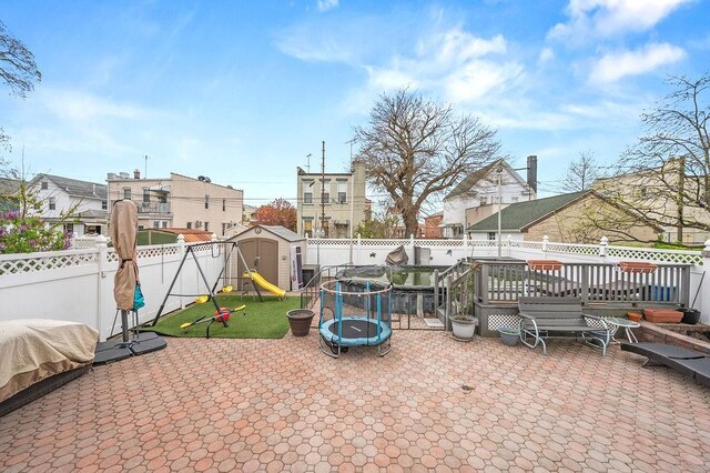 view of patio featuring a storage shed, a trampoline, a fenced backyard, an outbuilding, and a wooden deck