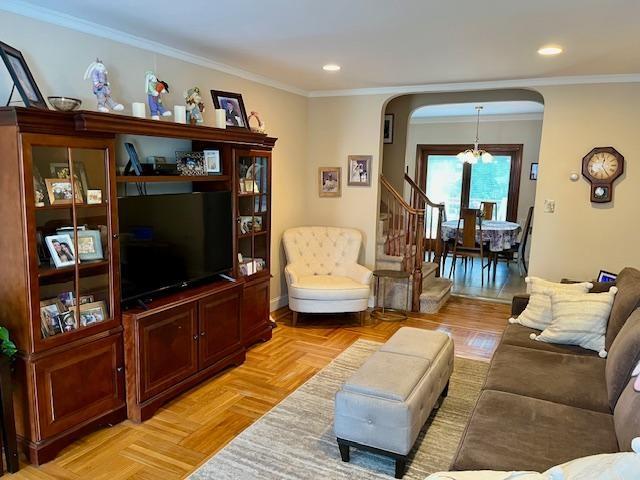 living room featuring arched walkways, recessed lighting, a chandelier, crown molding, and stairs