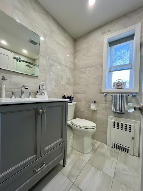 bathroom with radiator heating unit, tile walls, toilet, vanity, and marble finish flooring