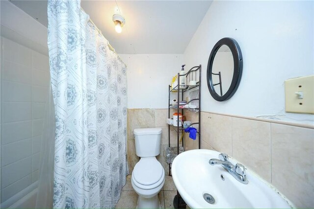 2939 Brighton 3rd St, Brooklyn, NY 11235 - full bathroom with a sink, toilet, a wainscoted wall, tile walls, and a shower with curtain