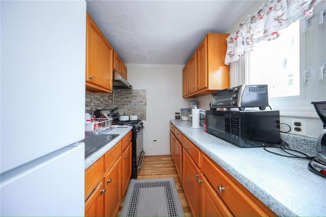 2939 Brighton 3rd St, Brooklyn, NY 11235 - kitchen featuring decorative backsplash, light countertops, under cabinet range hood, brown cabinets, and black appliances