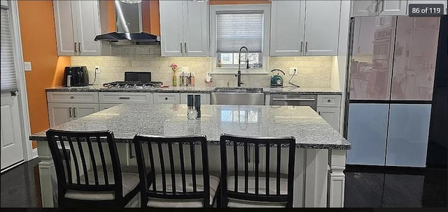kitchen featuring appliances with stainless steel finishes, wall chimney exhaust hood, a breakfast bar area, a sink, and decorative backsplash