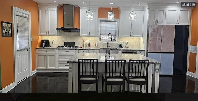 kitchen featuring wall chimney range hood, a sink, baseboards, white cabinetry, and recessed lighting
