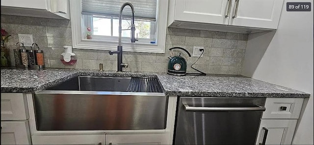 kitchen with dishwasher, white cabinets, tasteful backsplash, a sink, and dark stone counters