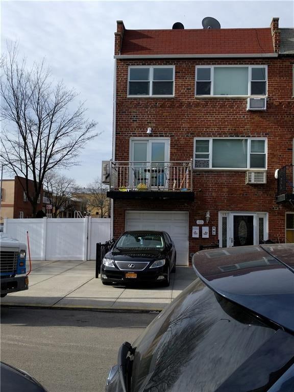 view of property featuring a balcony, concrete driveway, fence, a garage, and brick siding