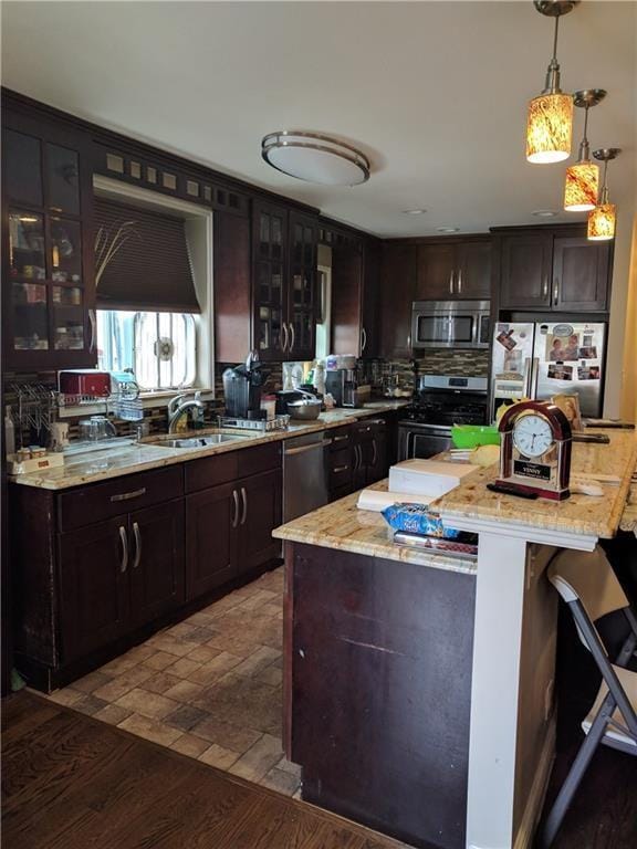 kitchen featuring stainless steel appliances, a sink, glass insert cabinets, light stone countertops, and hanging light fixtures
