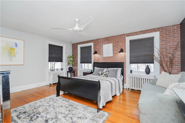 bedroom with baseboards, brick wall, radiator heating unit, and light wood-style floors