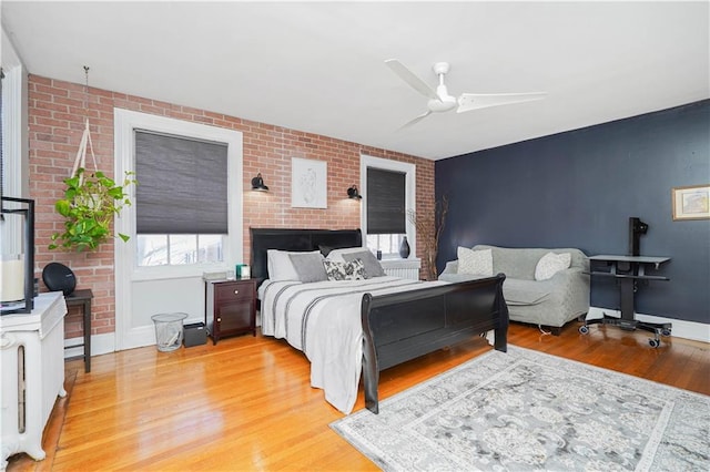 bedroom with baseboards, ceiling fan, light wood-type flooring, and brick wall