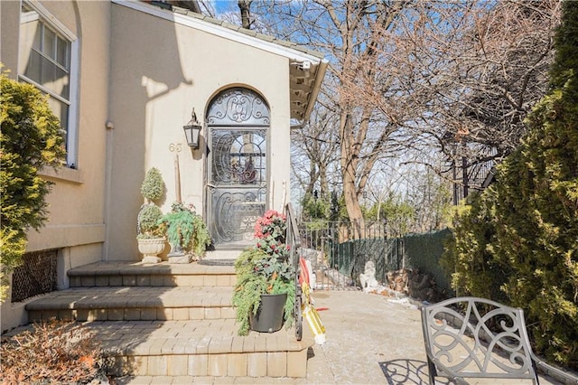 entrance to property featuring fence and stucco siding