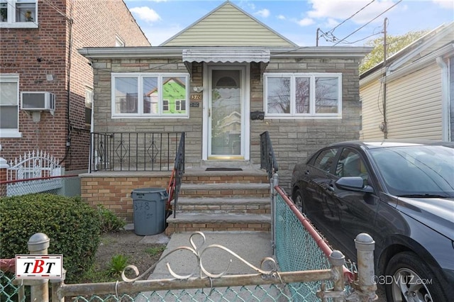 view of front of home with stone siding, a wall mounted air conditioner, and fence