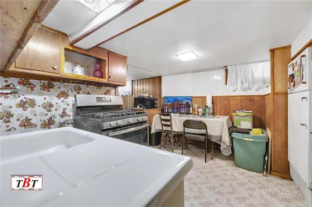 kitchen with stainless steel range with gas stovetop, light floors, black microwave, and brown cabinetry