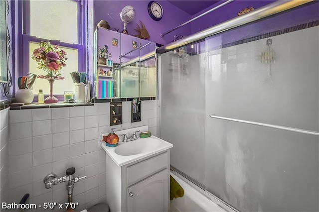 bathroom with enclosed tub / shower combo, vanity, and tile walls
