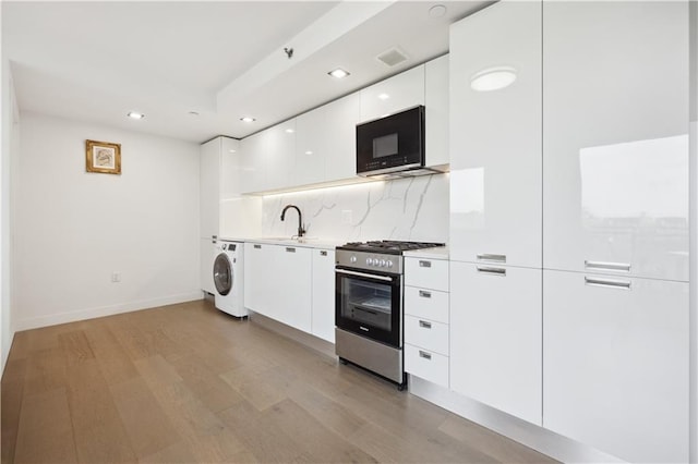 623 H Ave Unit 7C, New York, NY 11230 - kitchen with stainless steel range with gas cooktop, black microwave, modern cabinets, washer / clothes dryer, and white cabinetry