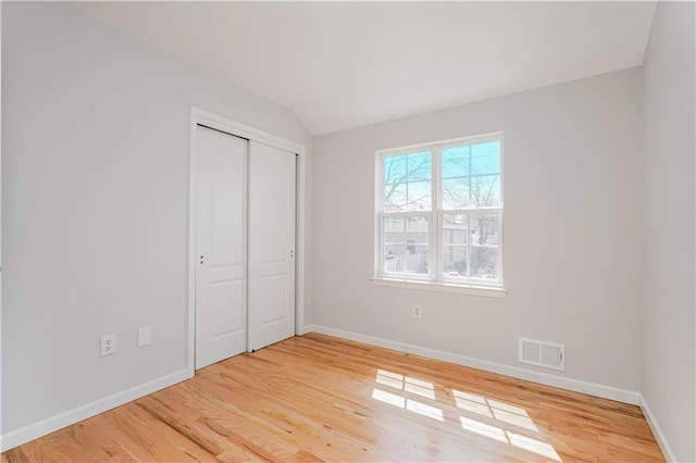 unfurnished bedroom with lofted ceiling, visible vents, baseboards, and light wood-style floors