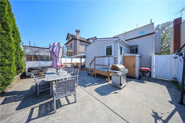 view of patio with fence, a gate, outdoor dining area, and a grill
