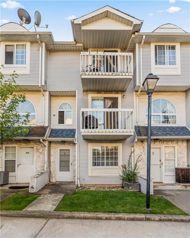 view of property featuring central air condition unit, stone siding, and a balcony