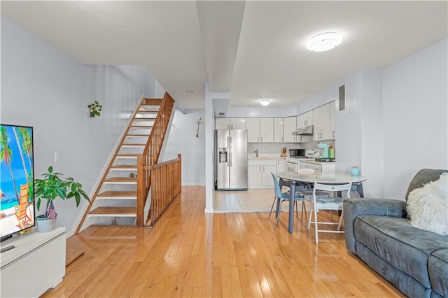 living room with stairs, visible vents, baseboards, and light wood-type flooring