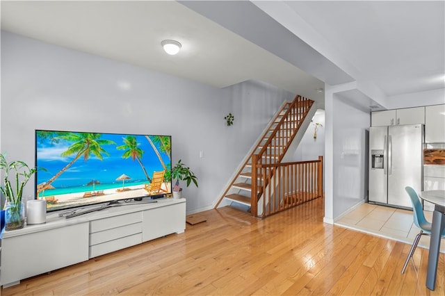 living room featuring stairs, light wood-style flooring, and baseboards
