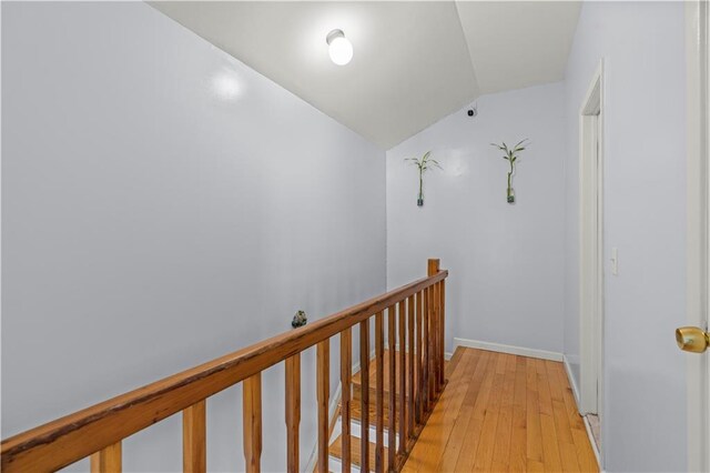 hallway featuring baseboards, light wood finished floors, an upstairs landing, and lofted ceiling
