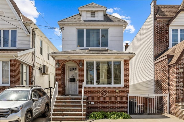 traditional style home featuring an AC wall unit, fence, and brick siding