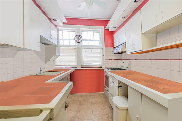 kitchen with ceiling fan, tasteful backsplash, gas stove, tile counters, and under cabinet range hood