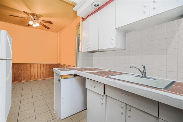 kitchen featuring a ceiling fan, light tile patterned floors, light countertops, white cabinets, and a sink
