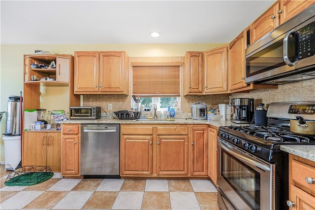 kitchen with a sink, appliances with stainless steel finishes, backsplash, and light stone countertops