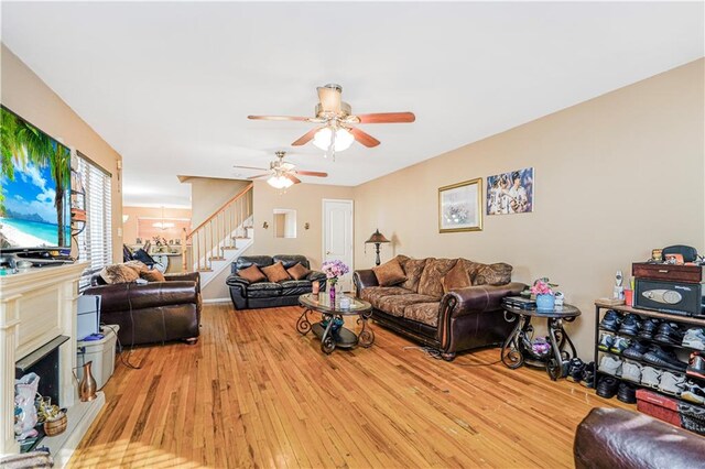 living area with wood-type flooring, a ceiling fan, stairs, and a fireplace with raised hearth