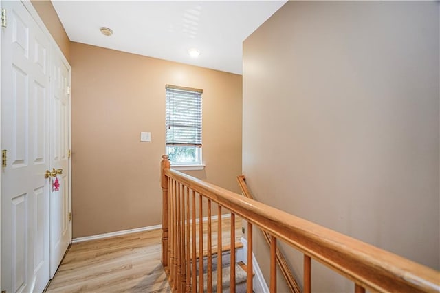 hall with baseboards, light wood finished floors, and an upstairs landing