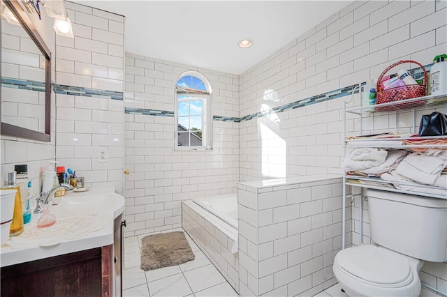 bathroom with tile patterned flooring, vanity, toilet, tile walls, and tiled tub