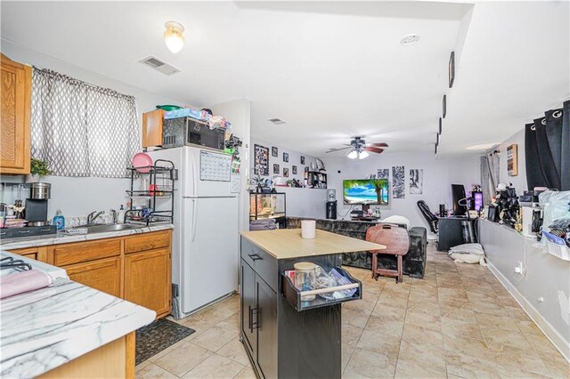 kitchen featuring visible vents, freestanding refrigerator, ceiling fan, light countertops, and a sink